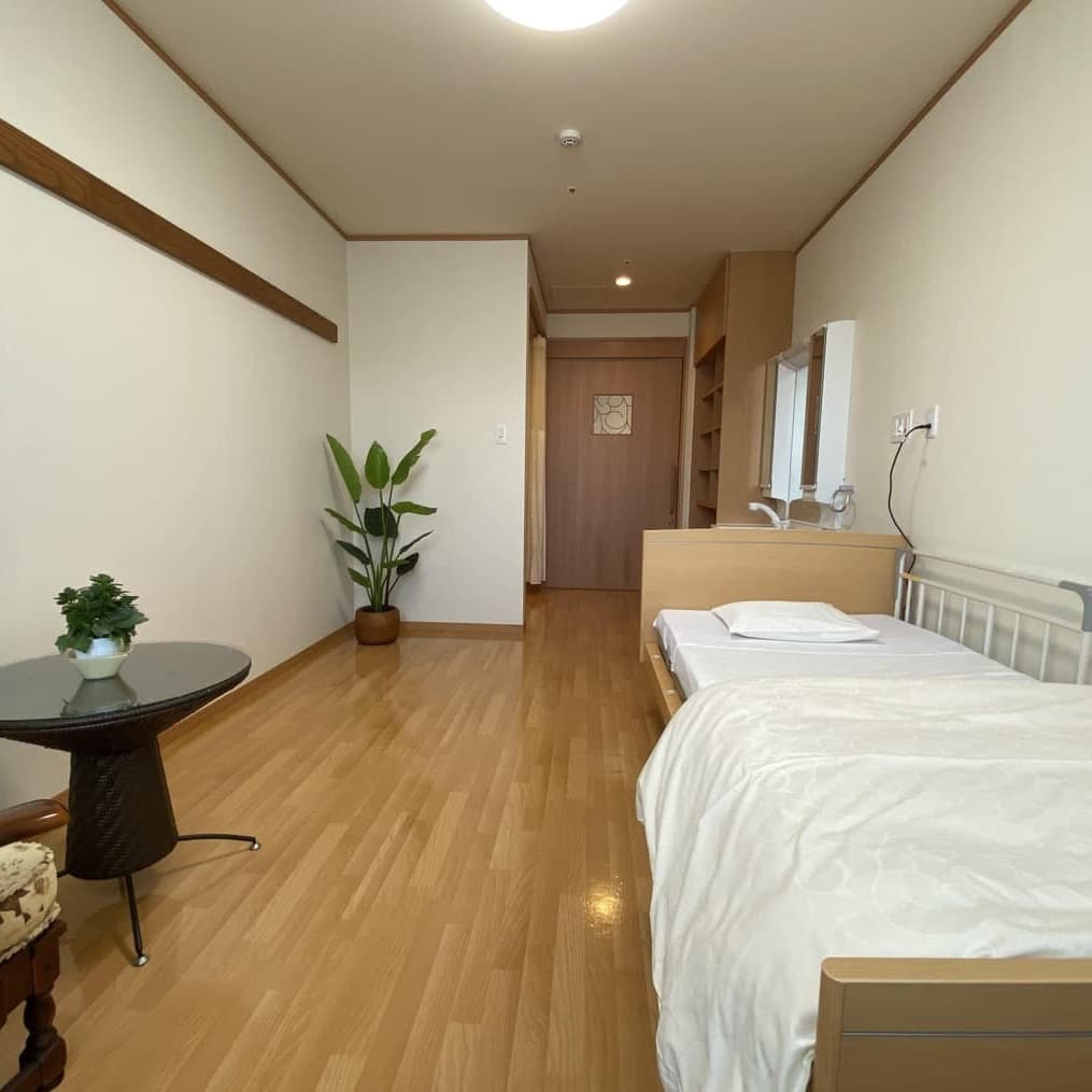 明るい居室。ベッド、洗面台、植物など整備された空間。